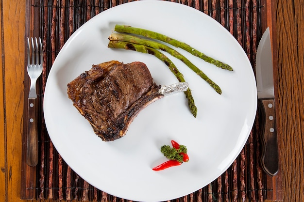 Gegrilde vleesribben op een witte plaat met tomaten bieslook en donkere hete saus aan boord