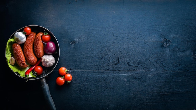 Gegrilde worstjes in een pan met verse groenten Houten op het zwarte oppervlak Bovenaanzicht