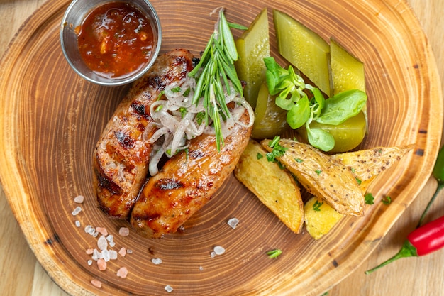 Gegrilde worstjes in honing en biersaus geserveerd in een houten plank met kruiden, gebakken aardappel, gepekelde komkommers en kool. Duitse, Beierse thuiskeuken. Selectieve aandacht