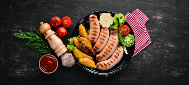 Gegrilde worstjes met aardappelen en groenten op een zwarte stenen achtergrond Vlees Bovenaanzicht Gratis kopieerruimte