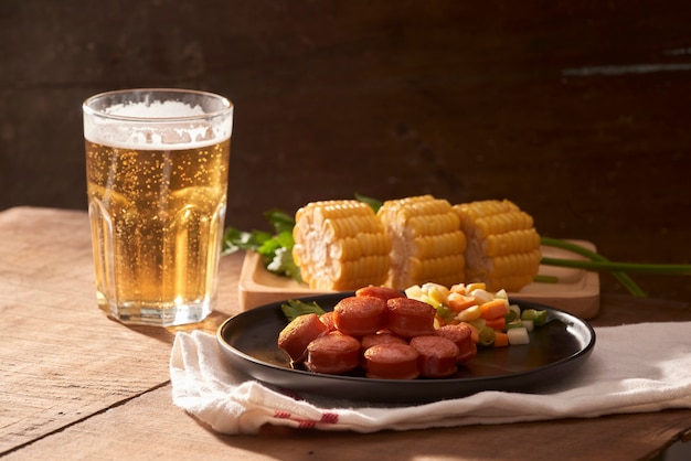 Gegrilde worstjes met glas bier op houten tafel met kopieerruimte.