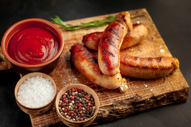 Gegrilde worstjes met kruiden, ketchup en rozemarijn op een stenen tafel, klaar om te eten