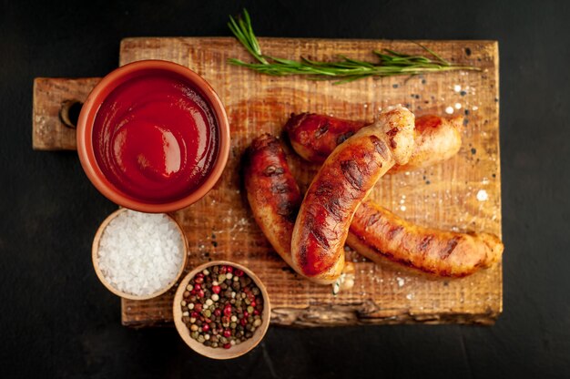 Gegrilde worstjes met kruiden, ketchup en rozemarijn op een stenen tafel, klaar om te eten