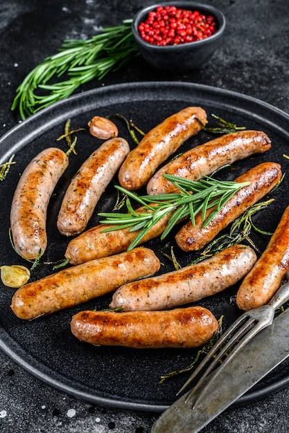 Gegrilde worstjes met rozemarijnkruiden, rundvlees en varkensvlees. Zwarte achtergrond. Bovenaanzicht.