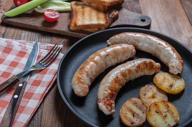 Gegrilde worstjes op koekenpan, gebakken aardappelen. Rauwe groenten op snijplank, keukenoppervlak. Selectieve aandacht