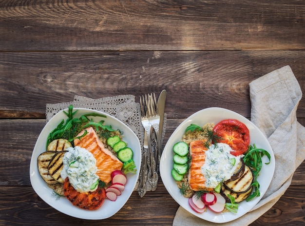 Gegrilde zalm, aubergines en tomaten met quinoa en tzatzikisaus op rustieke houten achtergrond. Gezond diner. Bovenaanzicht.