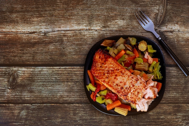 Gegrilde zalm met Aziatische roerbakgroenten op zwarte plaat met vork. Kopieer ruimte. Bovenaanzicht.