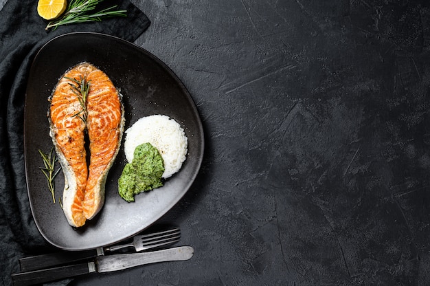 Gegrilde zalm steak gegarneerd met rijst en spinazie. Zwarte achtergrond. Bovenaanzicht. Ruimte voor tekst