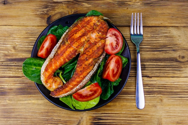 Gegrilde zalm steak met spinazie en tomaten op houten tafel bovenaanzicht