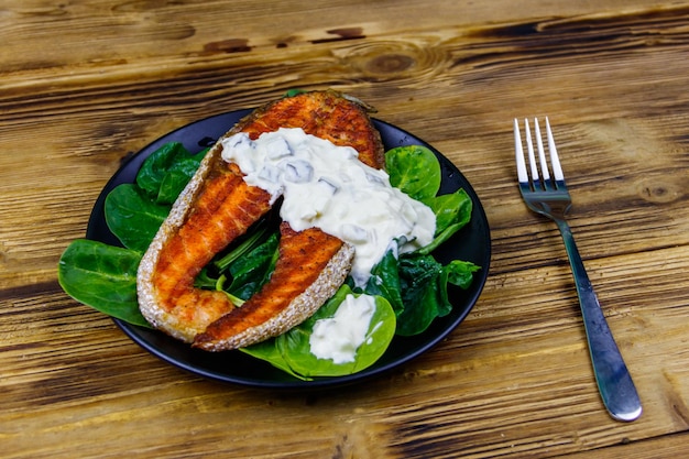 Gegrilde zalmsteak met spinazie en tartaarsaus op houten tafel