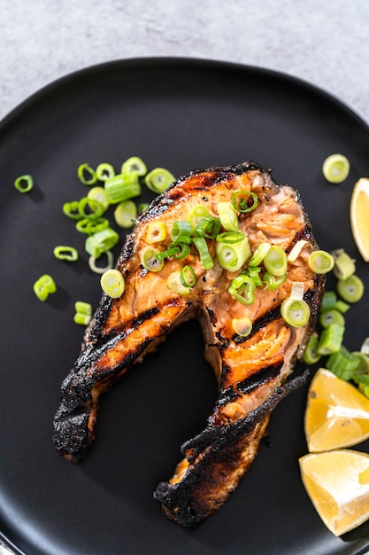 Gegrilde zalmsteaks gegarneerd met groene uien op een zwarte plaat