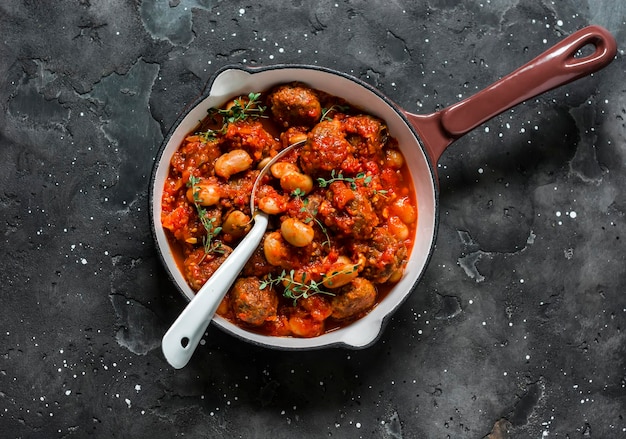 Gehaktballen en bonenstoofpot in tomatensaus met aromatische kruiden en specerijen in een koekenpan op een donkere achtergrond bovenaanzicht