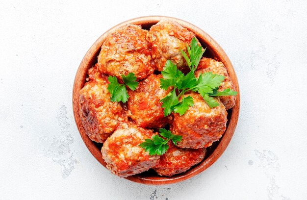 Gehaktballen in tomatensaus in houten kom op witte keukentafel achtergrond specerijen en kruiden Heerlijk thuis koken Bovenaanzicht