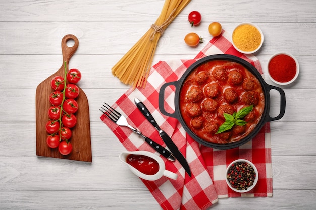Gehaktballen in tomatensaus met kruiden in een koekenpan en cherrytomaatjes op een snijplank