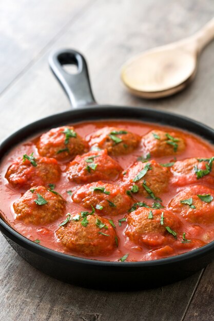 Gehaktballen met tomatensaus in ijzeren koekenpan op houten tafel