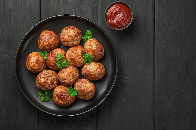 Gehaktballetjes met basilicum en tomatensaus op een zwarte achtergrond. Bovenaanzicht, kopieer ruimte.