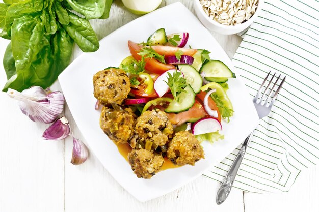 Gehakte gehaktballen met spinazie, havermout en groene uien in tomatensaus, groentesalade in een bord, servet op houten plankachtergrond van bovenaf