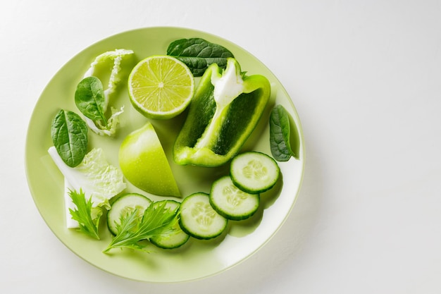 Gehakte groene groenten en fruit in een groene plaat. Verse groene dieetvoeding op witte achtergrond. Gezond vegetarisch voedselconcept. Ruimte kopiëren. Bovenaanzicht