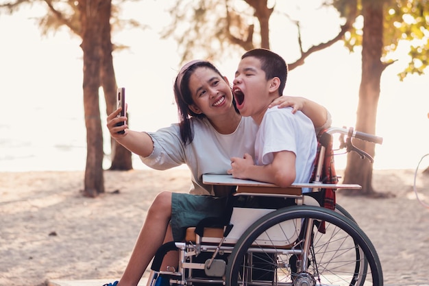 Gehandicapt kind op rolstoel glimlach smartphone gebruiken met ouder op het strand levensstijl van speciaal kind