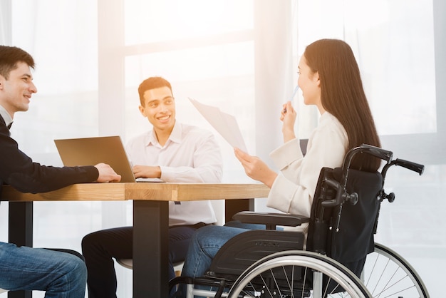 Gehandicapte jonge onderneemsterzitting op rolstoel die met zijn mannelijke collega in bureau bespreken