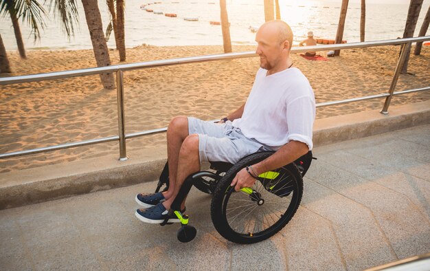 Gehandicapte man in een rolstoel beweegt op een helling naar het strand.