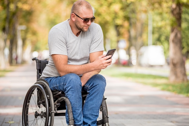 Gehandicapte man in rolstoel bij het parksteeg gebruikt een smartphone