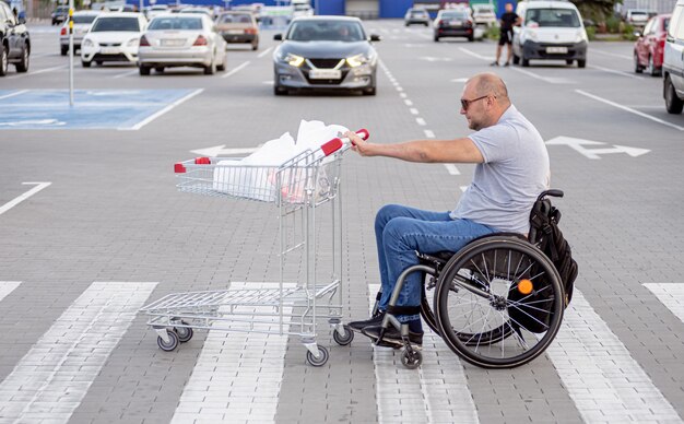 Gehandicapte man in rolstoel die kar voor zich uit duwt bij supermarktparkeren