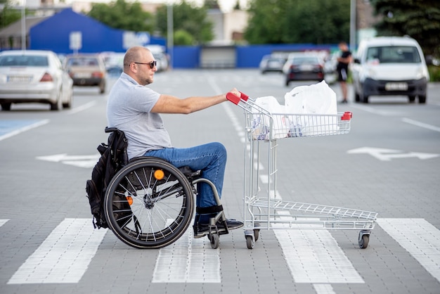 Gehandicapte man in rolstoel die kar voor zich uit duwt bij supermarktparkeren