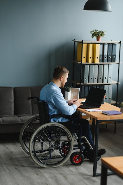 Gehandicapte persoon in de rolstoel werkt op kantoor op de computer Hij lacht en is gepassioneerd over de workflow
