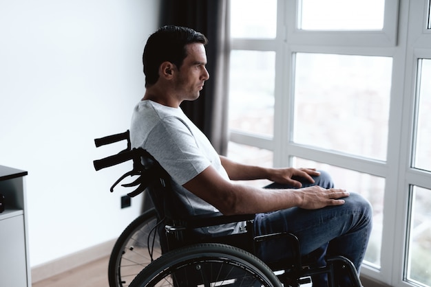 Gehandicapte persoon zit in rolstoel tegen raam.