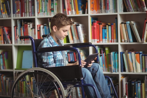 Gehandicapte schooljongen met behulp van digitale tablet in bibliotheek