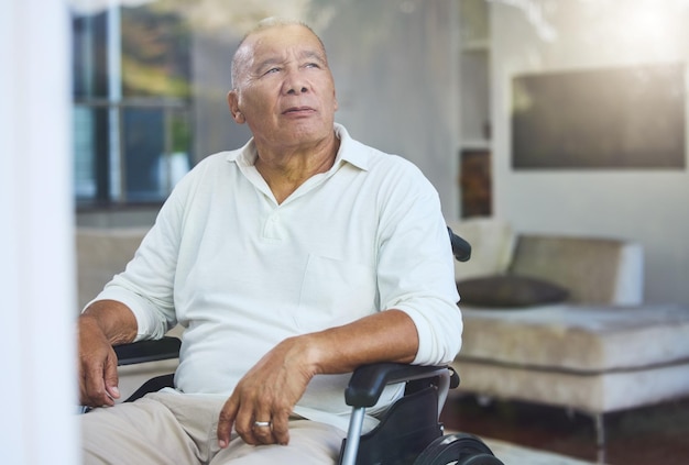 Gehandicapte trieste en oudere man die denkt aan een ongeluk in een rolstoel bij het raam in de woonkamer van zijn huis Oudere man met een depressie, handicap en pensioenidee in een verpleeghuis