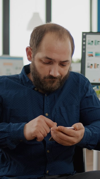 Gehandicapte, verlamde geïmmobiliseerde ongeldige jonge werknemer browsen op smartphone tijdens werktijd typen, zoeken zittend in een rolstoel. divers team dat financieel project bespreekt, statistieken controleert