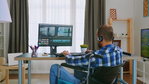 Gehandicapte video-editor in rolstoel die vanuit huis werkt met een koptelefoon.