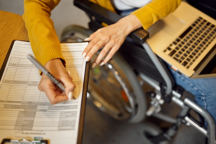 Foto gehandicapte vrouwelijke student in rolstoel schrijft in notitieboekje, handicap, universiteitsbibliotheek interieur op achtergrond. gehandicapte vrouw studeert op de universiteit, verlamde mensen krijgen kennis