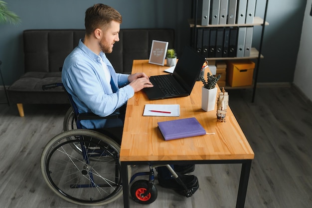 Gehandicapte zakenman zittend op rolstoel en het gebruik van de computer op kantoor