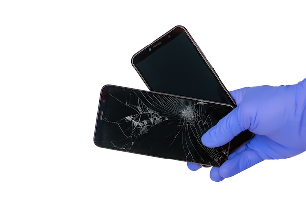 Foto gehandschoende hand houdt een gebroken smartphone met een gebarsten scherm van een mobiele telefoon en een nieuw scherm van een mobiele telefoon op een witte ruimte