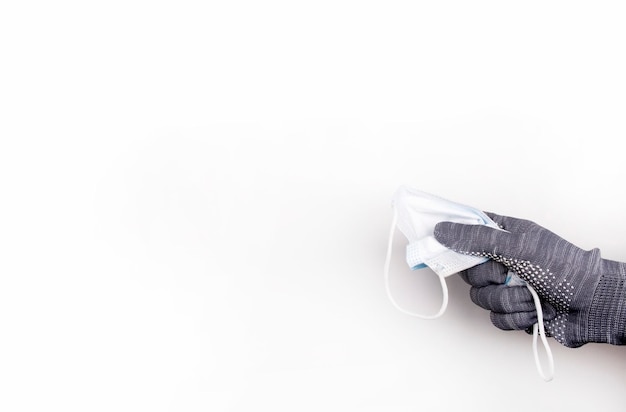 gehandschoende hand knijpt een gebruikt masker op een witte achtergrond. Afvalinzameling. Milieubescherming