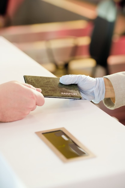 Foto gehandschoende hand van vrouwelijke receptioniste die bij de balie staat en het paspoort van de mannelijke passagier teruggeeft na registratie vóór de vlucht