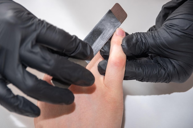 Gehandschoende handen van een bekwame manicure die de nagels van een jonge vrouw vijlt met een nagelvijl Handen tijdens een manicure-verzorgingssessie