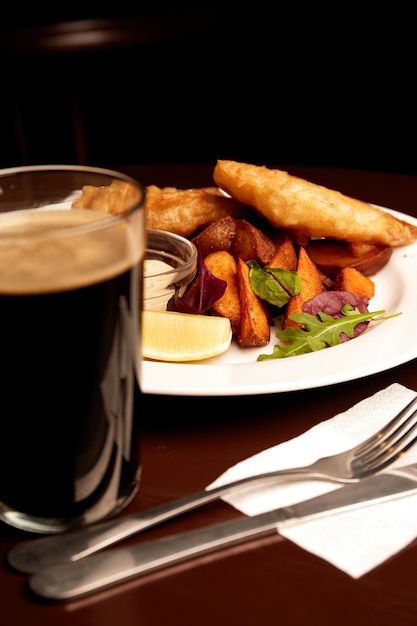 Gehavende vis op een bord met chips op een houten tafel in de pub en een pint stevige ongezonde voeding