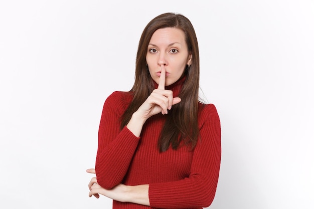 Geheime jonge brunette vrouw meisje in casual rode kleding poseren geïsoleerd op een witte achtergrond in de studio. Mensen levensstijl concept. Bespotten kopie ruimte. Zeg stil, wees stil met de vinger op de lippen, shhh gebaar.