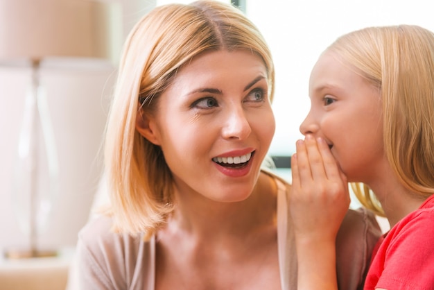 Geheimen delen met mama. gelukkige moeder en dochter die geheimen delen terwijl ze samen thuis zitten