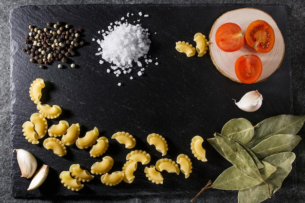 Gehele korrel ruwe Italiaanse deegwaren en ingrediëntensamenstelling op de zwarte rustieke achtergrond van de leisteen