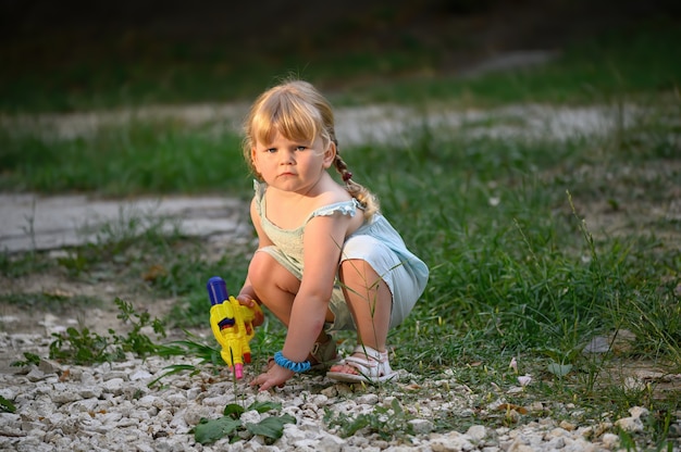 Gehurkt blond meisje met waterpistool speelt de geheimagent