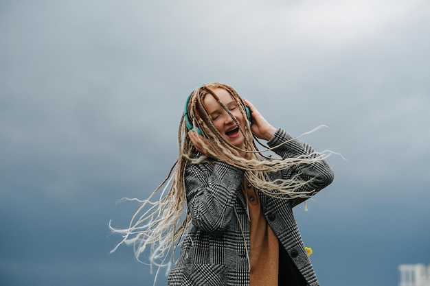 Gehypte tienermeisje met dreadlocks die naar muziek luistert en haar hoofd schudt