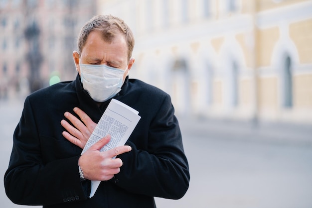 Geïnfecteerde man draagt medisch masker, heeft constant hoesten, symptomen van Covid-19, houdt opgerolde krant vast, poseert buiten in de stad, heeft isolatie nodig om de verspreiding van het coronavirus te stoppen. Preventieve maatregelen