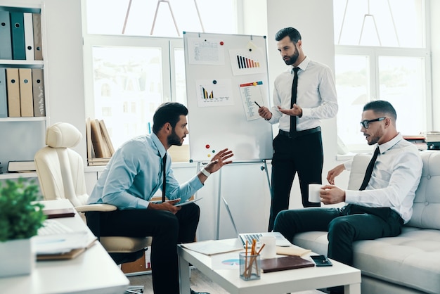 Geïnspireerd om hard te werken. Jonge moderne man in formalwear die een zakelijke presentatie geeft met flipchart terwijl hij op kantoor werkt