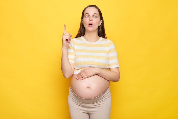 Geïnspireerde opgewonden blanke zwangere vrouw in casual kleding poseert geïsoleerd op een gele achtergrond met een uitstekend idee die de vinger omhoog tilt met een verbaasd gezicht