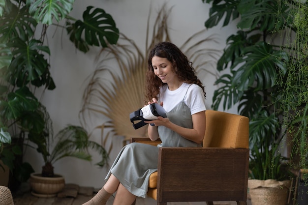 Geïnteresseerde jonge vrouw houdt een bril vast voor virtual reality-simulatie die in de tuin van het huis zit